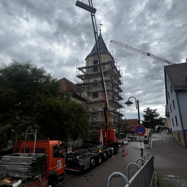 Kran hebt Gerüstmaterial an Kirchturmspitze